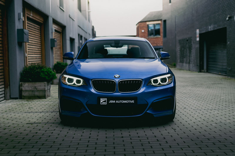 A photograph of a dark blue BMW sports car parked outside Scandinavian buildings