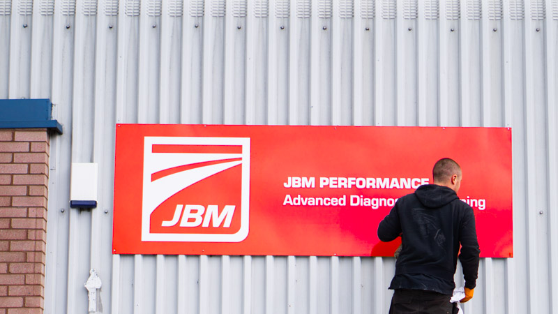 A photograph of a man installing a sign for JBM performance in Sheffield