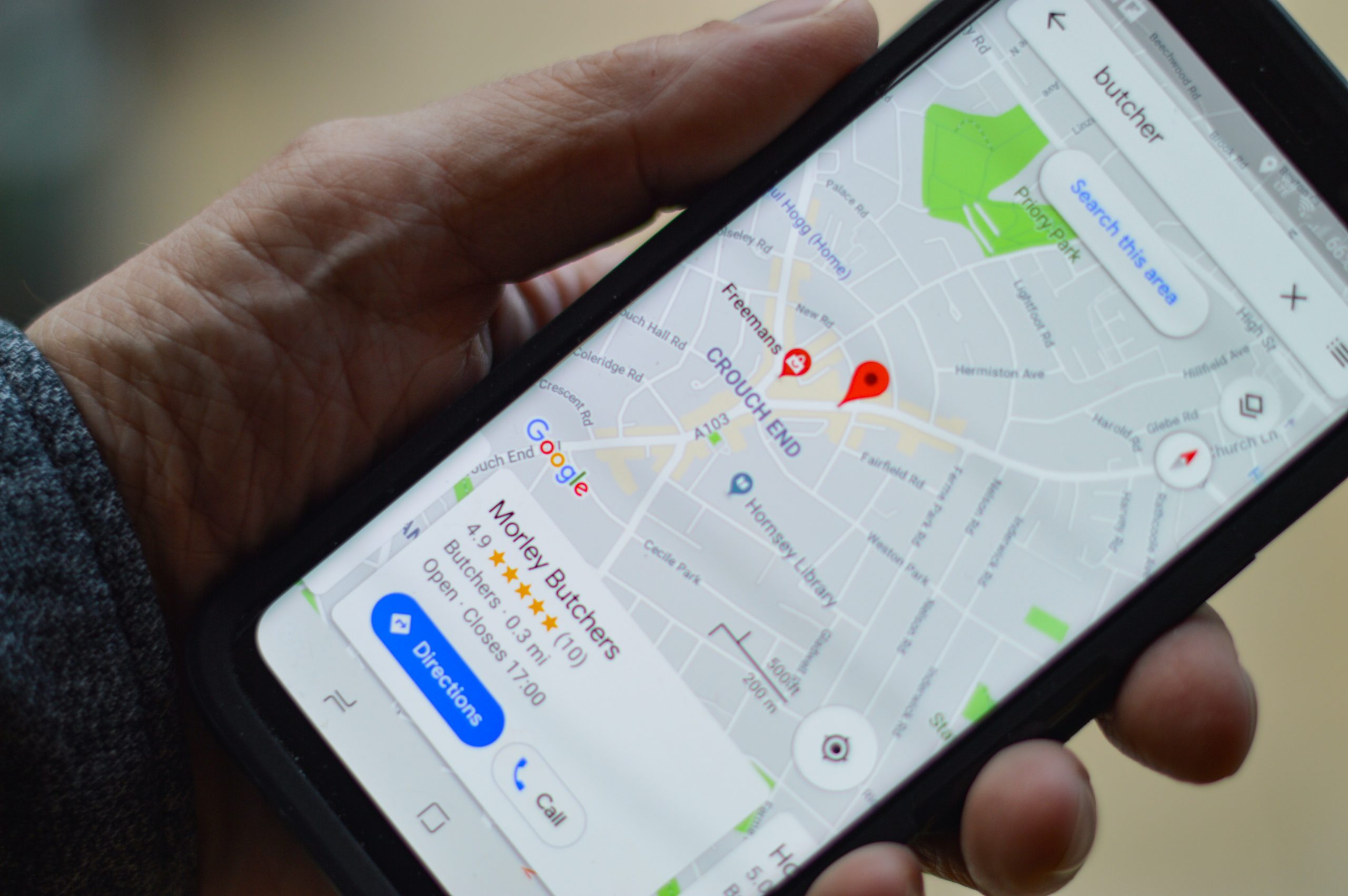A photograph of a hand holding an iPhone showing a Google maps search for a butcher