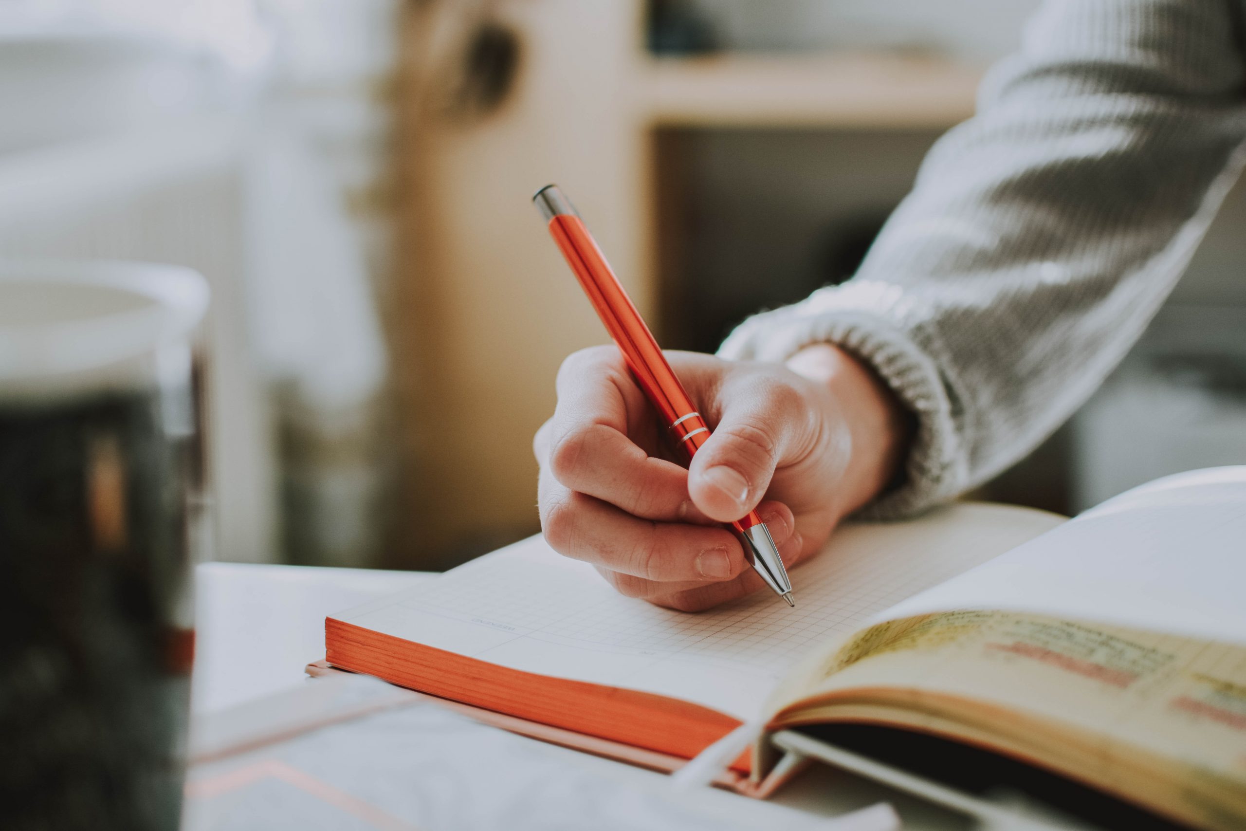 A photograph of a women holding a pen and making an entry into a journal