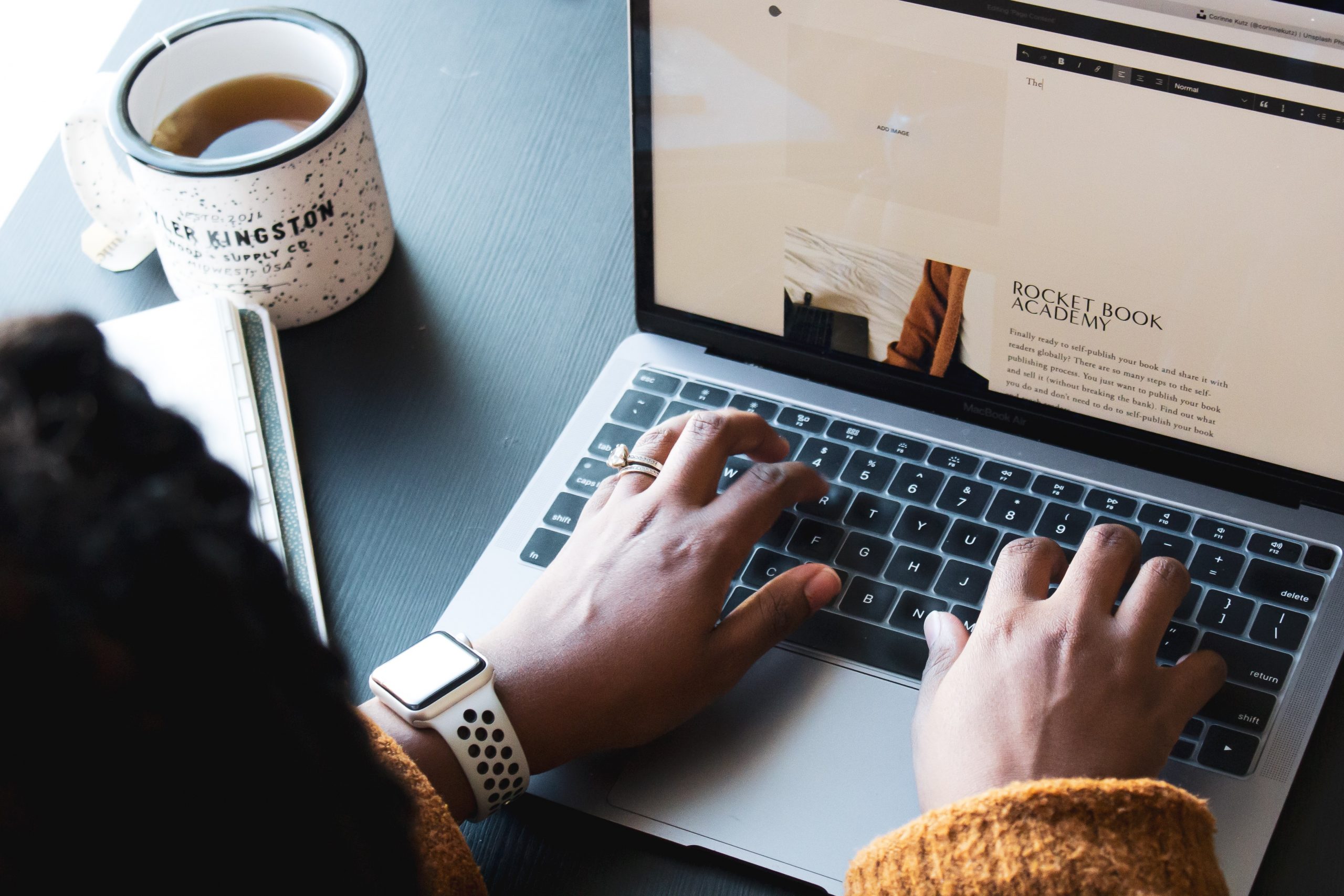 A photograph of a woman using a MacBook Pro to edit a Squarespace site on a black desk next to a cup of coffee