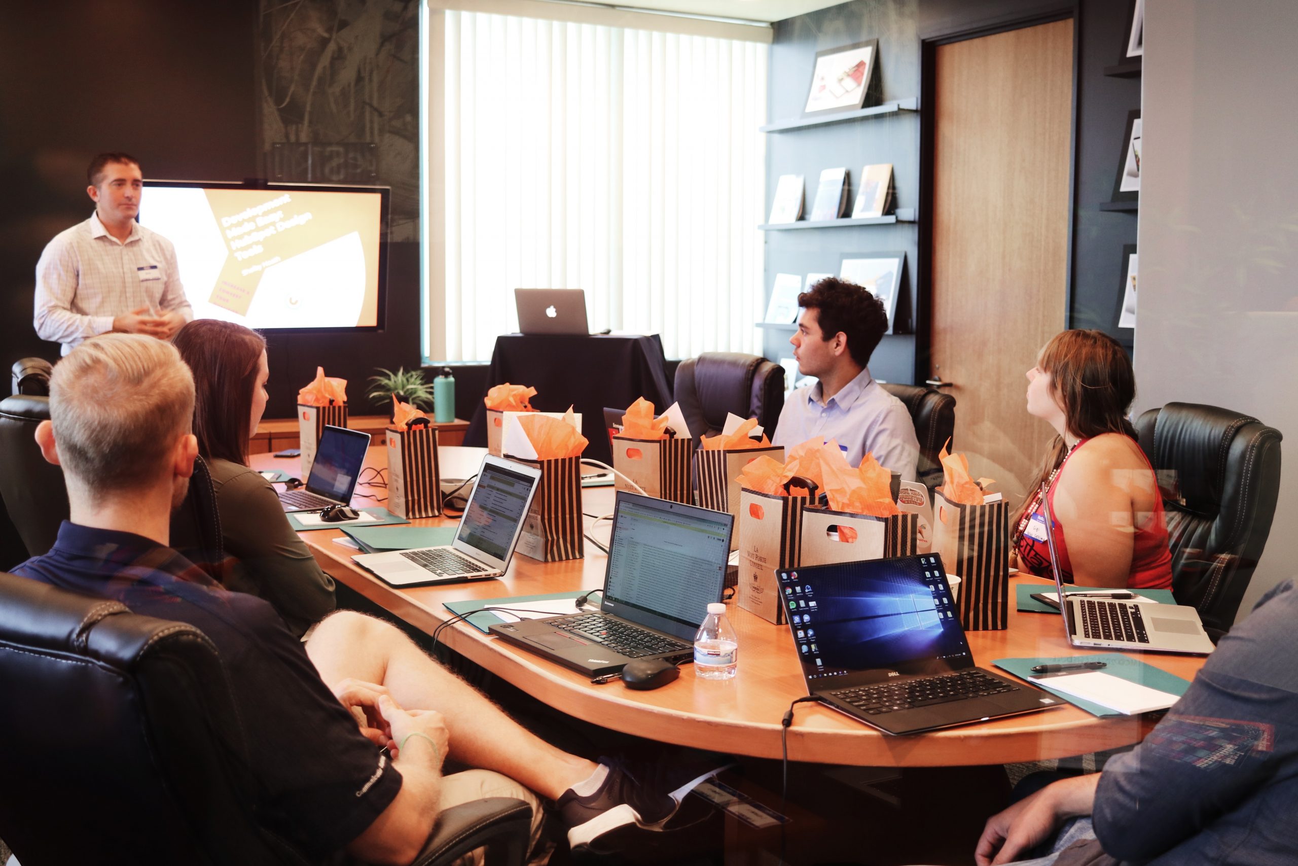 A photograph of six people around a wooden desk listening to a presentation at work