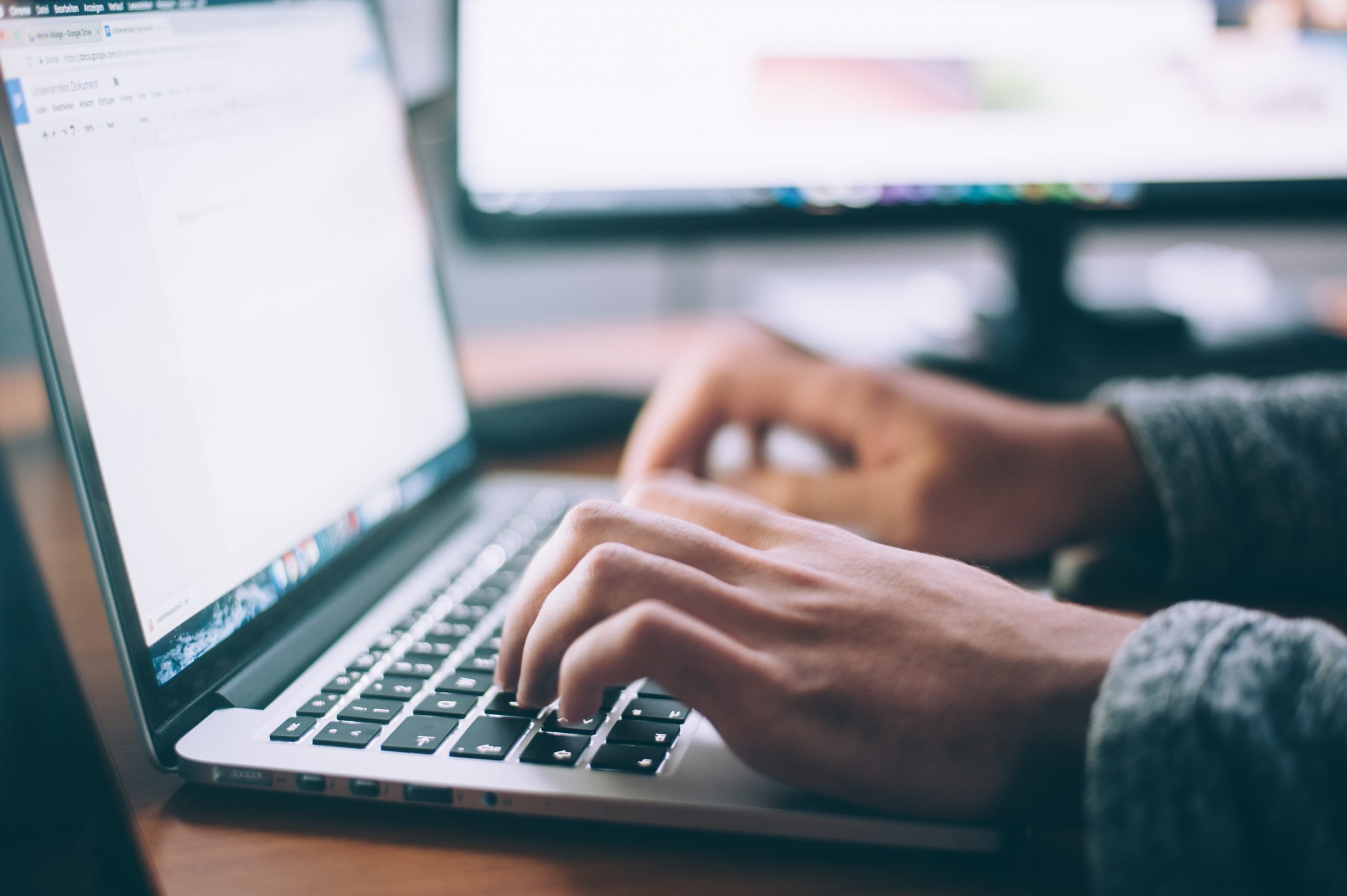 A photograph of a woman using a laptop in front of a blurred out computer screen